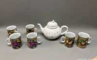 Full set of six Limoges mugs arranged around a white Villeroy & Boch teapot with blue floral accents on grey background.