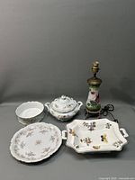 All items in the lot displayed together against a gray background: porcelain lamp, lidded casserole dish, charger plate, bowl, and rectangular tray