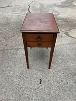 Front view of the wooden end table with two drawers and tapered legs, showing surface wear on the top.