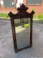 Full view of Victorian Eastlake wall mirror showing dark wooden frame with carved crest and side columns in outdoor lighting.
