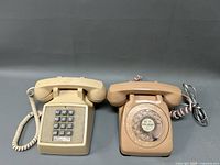 Two vintage telephones on a grey surface, one push button phone on the left and one rotary dial phone on the right.