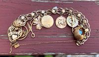 Full view of the 10K gold charm bracelet with multiple charms on red wooden surface