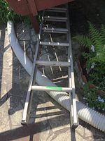 Full length view of the aluminum ladder showing rectangular rungs and metallic finish with dirt and wear.