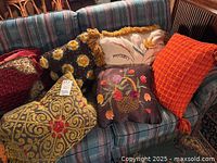 Seven artisan throw pillows arranged on a blue plaid couch, showing the variety of textiles and colors in the lot.