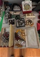 Assortment of vintage costume jewelry brooches and beaded jewelry pieces, displayed in boxes and on table showing floral and leaf motifs and other designs.