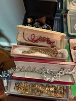 Overall view of black jewelry box with rings and charms, plus three presentation boxes containing necklaces and bracelets.