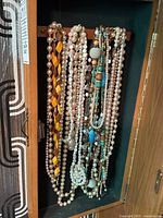 Photo of multiple necklaces hanging inside a jewelry box door including faux pearl and wood bead necklaces.