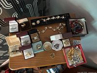 Overview of assorted jewelry on wood table showing rings in boxes, brooches, necklace and other pieces