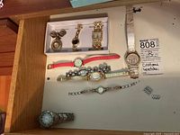Lot of 9 costume watches on table showing various designs including boxed watches and wrist strap watches
