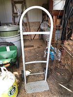 Metal dolly hand truck in a barn or shed, showing curved handle, wheels and flat front base platform.