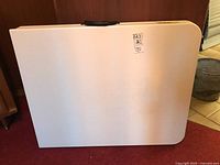 Folding table folded in half showing smooth white resin top surface with a price sticker.