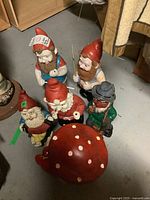Photo showing five plastic gnomes and one large red mushroom figurine with white spots on floor.