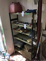 Full view of metal shelving unit containing five shelves with assorted hand and garden tools including hammers, saws, a red gas can on top shelf, rakes, and shovel handles visible.