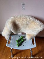 Bathroom chair with plastic seat and back and metal frame, cream lambskin rug draped over the backrest, green dumbbell weights on seat.