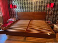 Full view showing headboard, frame and slatted base on hardwood floor against patterned wallpaper.