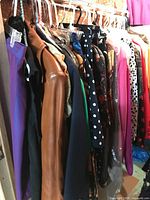 Side view of clothing rack showing a variety of hung women's garments including a tan leather jacket, a navy polka dot blouse, and other colorful items.