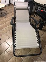 Frontal view of the lounge chair laid flat, showing beige fabric, black frame, and pillow.