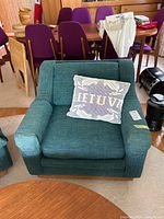 Front view of teal slub fabric club chair showing seat cushion, armrests and decorative throw pillow