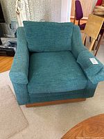 Front view of teal slub upholstered armchair with loose seat and back cushions, wood base on casters