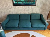 Front view of teal slub-fabric three-seat sofa with loose cushions and low wood base on casters.