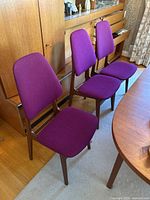 Four MCM teak dining chairs in a row showing frame and upholstery color