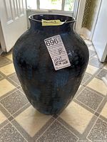 Tall floor vase, dark brown and blue glaze with textured surface. Photographed from the front showing floor tiles beneath and room background.
