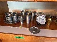 Full shelf view showing pewter cups, small handling cups, glasses, pitcher, tray, and coasters.