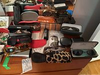 Overview photo showing 13 pairs of glasses and sunglasses with their respective cases arranged on a wooden surface.