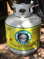 Close-up photo of white propane tank with yellow Tank Traders label showing logo and branding.