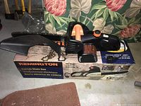 Side view of Remington electric chainsaw with safety guard and chain resting on box.