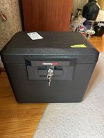 Front view of black SentrySafe with keys in lock and yellow tag on top right corner