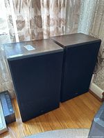 Pair of vintage wood speakers side by side showing front black fabric grille and wood finish on top.