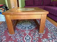 Side view of square teak coffee table showing thick legs and wood grain with tile insert on top.