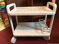 White plastic bar trolley with two shelves, four wheels, and molded bottle holder on bottom shelf.