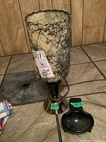 Full view of vintage MCM lamp with cylindrical textured lampshade and black gold-tone base, alongside black ashtray on tile floor