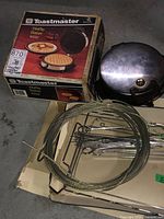 Toastmaster waffle maker in original box with kabob skewers and wire rack placed on floor