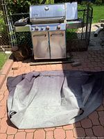 Weber Genesis grill standing on patio with grey protective cover laid out front
