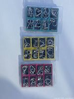 Three plastic trays (teal, yellow, red) each containing eight metal wire disentanglement puzzles, total 24 pieces