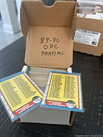 Open cardboard box showing large stack of 1989-90 O-Pee-Chee NHL cards and two checklist cards