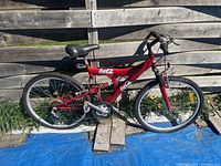 Left side view of entire bicycle leaning against wooden fence