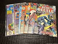 Front view of seven Blue Beetle comics in sleeves