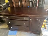 Front view of dark brown dresser showing three drawers and cabinet door