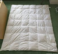 Full view of the white duck down duvet laid flat on a green carpet, showing box baffling sewn in square pattern.