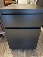 Front view of black-brown 2-drawer filing cabinet on wheels with closed drawers.