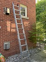 Extension ladder leaned against brick wall, fully extended length visible