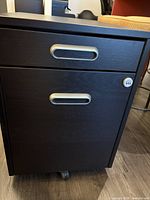 Front view of black-brown IKEA filing cabinet showing upper 2 drawers and combination lock on side.