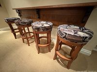 Four solid wood bar stools with circular padded swivel seats upholstered in vintage cigar motif fabric.
