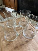 Four clear glass mugs arranged on a wooden table showing their size and delicate handles.