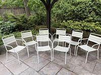 Eight white metal garden chairs arranged in garden setting