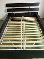 Full view of assembled bed frame showing wooden slat base and black-brown wood headboard with metal support braces.